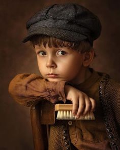 a young boy in a brown shirt is brushing his teeth with a wooden brush and looking at the camera