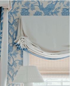 a bedroom with blue and white wallpaper, curtains and a lamp in the corner