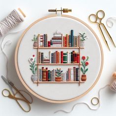 a cross stitch book shelf with books and flowers on it next to scissors, thread and spools