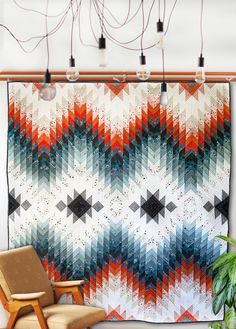 a chair sitting in front of a quilt hanging on a wall next to a potted plant