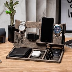 an iphone, watch, and other electronics in a wooden holder on a table with a plant