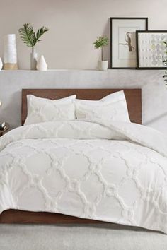 a bed with white comforter and pillows in a room next to a plant on the wall