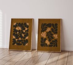 two framed art pieces sitting on top of a hard wood floor next to each other