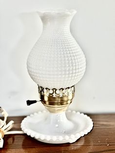 a white glass vase sitting on top of a wooden table next to a candle holder