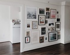 a wall with many pictures on it and a refrigerator in the backround next to it