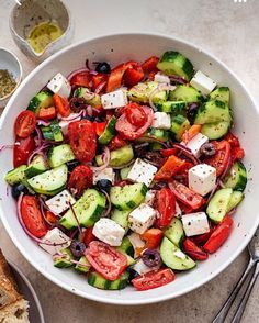 a white bowl filled with cucumber, tomato and feta cheese salad next to bread