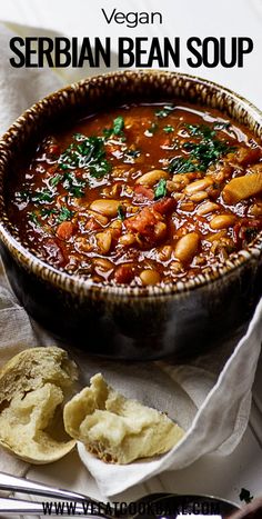 there is a bowl of bean soup with bread on the side and spoons next to it