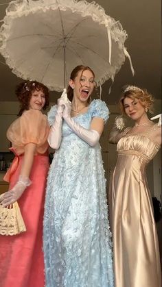 three women in dresses are holding an umbrella