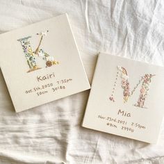 two personalized embroidered cards on top of a white bed sheet with the names and date