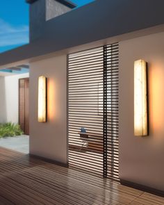 two lights on the side of a building next to a wooden floor and wall with an open door