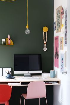 a desk with a computer on top of it next to a pink chair and yellow lamp