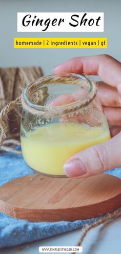 a person holding a glass jar filled with yellow liquid on top of a wooden board