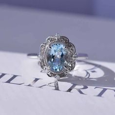 an oval cut blue topaz ring with filigrees on the sides, set in white gold