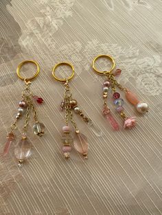 three pairs of key chains with charms attached to them sitting on a lace covered surface