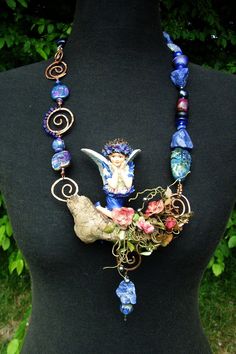 a necklace made with glass beads and other items is displayed on a mannequin