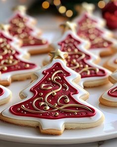 decorated christmas cookies on a white plate with red and gold decorations in the shape of trees