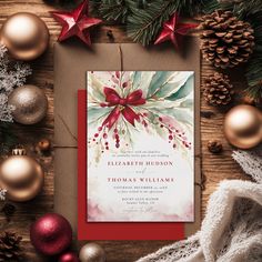 a red and white christmas card on top of a wooden table next to holiday decorations