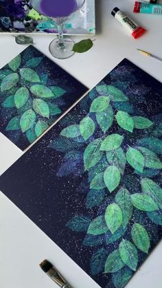 two paintings with green leaves on them next to paintbrushes and other art supplies