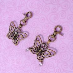 two metal butterfly charms on a pink background