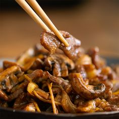 chopsticks picking up some food from a plate with meat and mushrooms on it