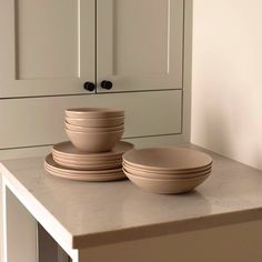 there are many plates and bowls on the counter top in front of white cupboards