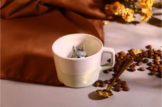 a coffee cup with a cat in it next to some coffee beans and a spoon