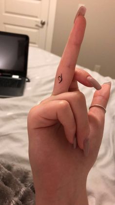 a person's hand with a small heart tattoo on their thumb and the middle finger