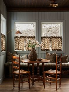 a table and chairs in a small room with two windows above the couch, next to a window seat