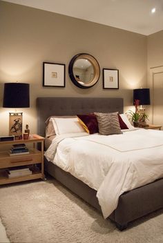 a large bed sitting in a bedroom next to two lamps and a mirror on the wall