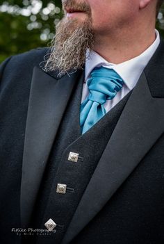 a man with a beard wearing a blue bow tie and black suit jacket, looking off to the side