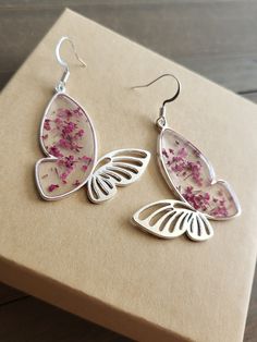 Beautifully Rose Pink flower earrings, elegant butterfly earrings with delicate, dried flowers inside. Silver butterfly earrings have silver finishing and hooks.  In earlier centuries, a gift of flowers was a meaningful gesture meant to portray the surrounding feelings involved, and show deep affection and appreciation for the receiver. It was known, Rose Pink was worn as a representation of luxury and wealth, as it was an expensive color worn by the upper class of society by privileged women of high stature. A gift of blushing rose pink flower earrings, complimented with gold, will surely bring a smile to her face. These burning pink~red floral earrings offer to be the most brilliant and unique jewelry piece in her jewelry box. Pink magenta flower earrings make a beautiful gift for brides Rose Pink Flower, Heather Flower, Succulent Flowers, Jewelry Silver Earrings, Pink Flower Earrings, Silver Butterfly Earrings, Magenta Flowers, Flowers Butterfly, Flower Butterfly