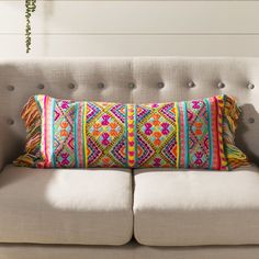 a couch with a colorful pillow on it in front of a white wall and potted plant