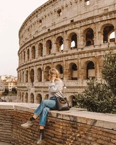 a woman is sitting on the wall in front of an old building talking on her cell phone