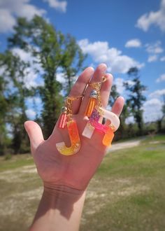 a person holding up their hand with some charms on it's fingers in front of the sky