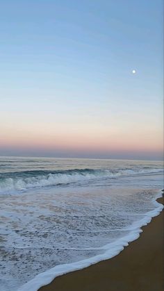 the ocean waves are rolling in and out on the beach as the sun is setting