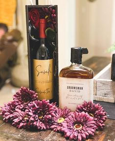 a bottle of booze next to some flowers on a table with a wooden box