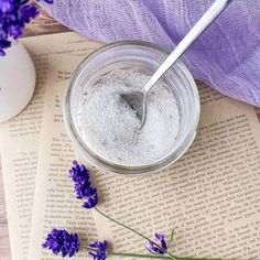 a spoon is in a jar with lavender flowers on top of an open book next to it