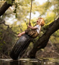 a young boy is swinging on a tire swing in the water while holding onto a rope