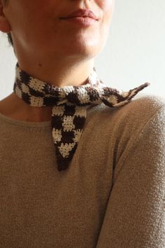 a woman wearing a brown sweater with a black and white flowered neck tie on her neck