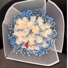 a bouquet of white roses and blue baby's breath in a clear plastic box