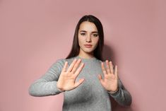 a woman is holding her hands up in front of her face while standing against a pink wall