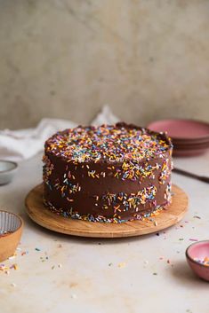 a chocolate frosted cake with sprinkles on a wooden plate next to other plates