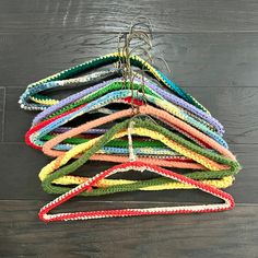 a pile of multicolored crocheted ties hanging from a hook on a wooden floor