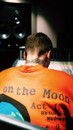 a man with his back to the camera wearing an orange shirt that says on the moon act i return hands