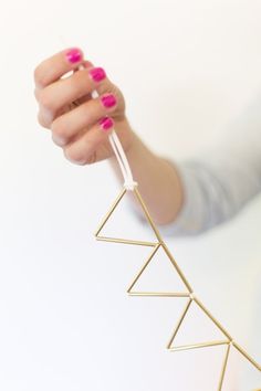 a woman is holding up a gold necklace with three triangles on it and pink nail polish