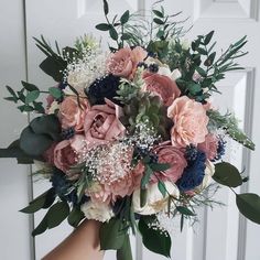 a bridal bouquet in front of a white door with greenery and pink flowers