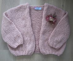 a pink knitted sweater with flowers on the front and back, sitting on top of a wooden floor