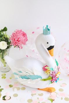 a white swan with a crown on its head next to flowers and confetti