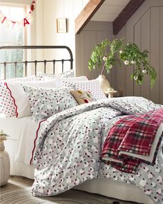 a bed with red and white sheets, plaid pillow cases and pillows on top of it