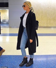 the blonde woman is wearing black boots and a long coat while walking through an airport